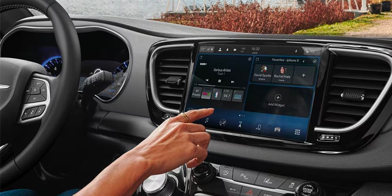 A hand interacting with a car's infotainment system, showing music, favorites, and "Add Widget" options on the screen.