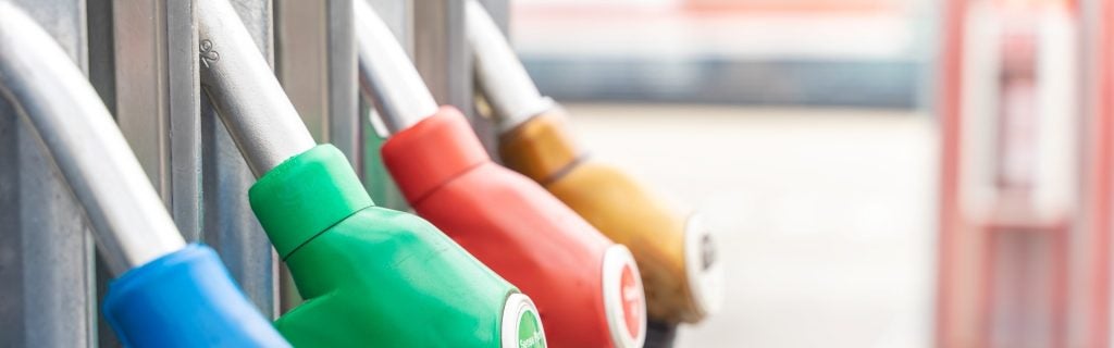 Four colorful fuel nozzles hanging at a gas station, from left: blue, green, red, and yellow.