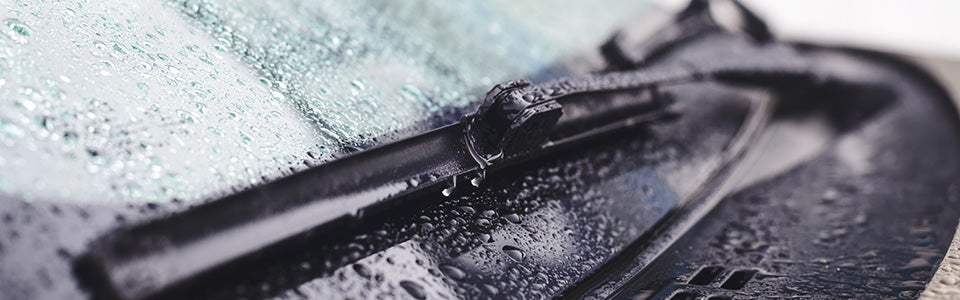 Close-up of a car windshield and wiper, covered in small raindrops.