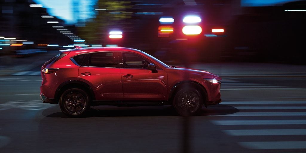Red CX-5 driving at night on a city street, with blurred lights in the background.