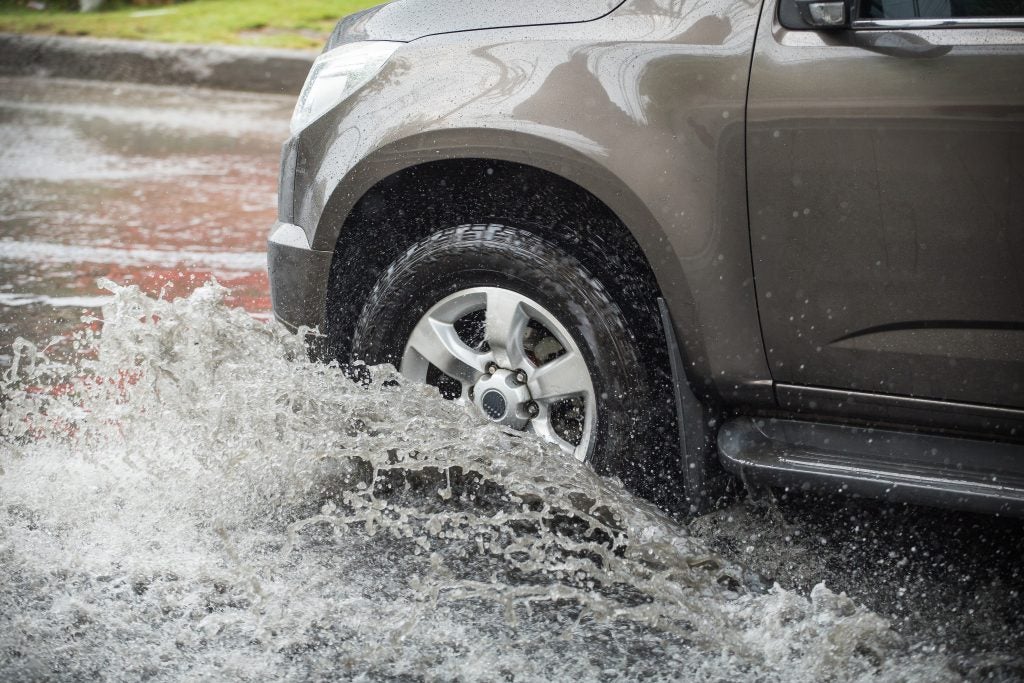 Front of a dark gray SUV driving through a deep puddle or flood water, creating a large splash.