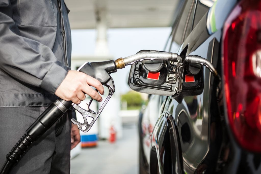 A person in a gray uniform filling a black car with gasoline at a gas station.