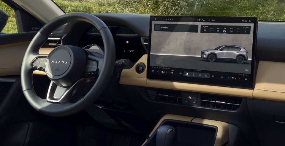 Interior view of a car looking towards the passenger side, with a steering wheel on the left and a large digital display on the right.