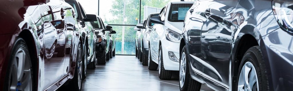 Row of various cars in a showroom, viewed from a low angle. Reflections in their shiny surfaces.