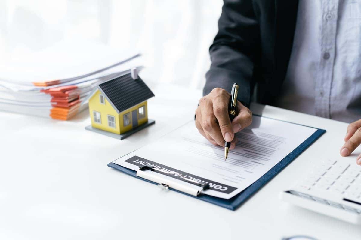 A hand holding a blue pen signs a document, with car keys resting on the paper.