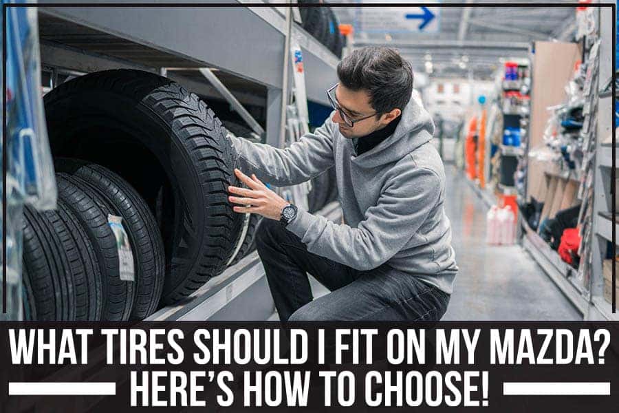 A man carries a tire with a new silver hubcap by rows of tires on shelves.
