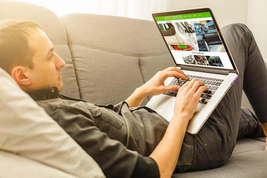 Men sitting on a white couch, looking at a laptop.
