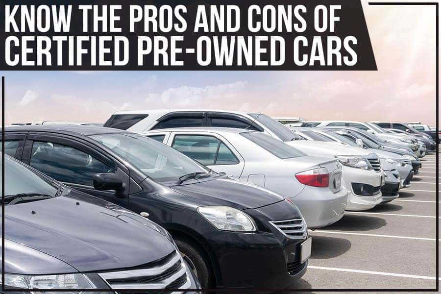 A line of new cars in a parking lot, with modern buildings in the background.
