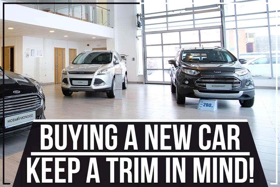 A large, silver GMC truck is parked inside a brightly lit dealership showroom with several desks and chairs to the right.