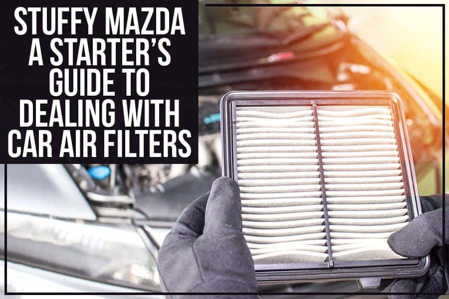 A gloved hand removes a rectangular car air filter from its casing in a car engine compartment.
