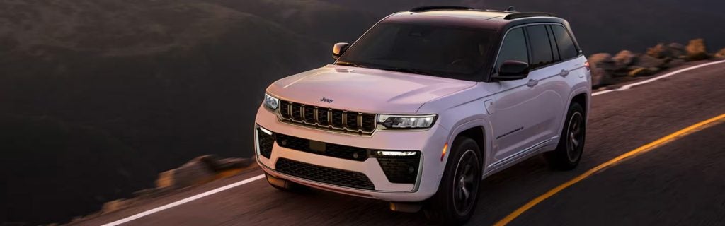 2026 Jeep Grand Cherokee driving on a scenic highway at sunset