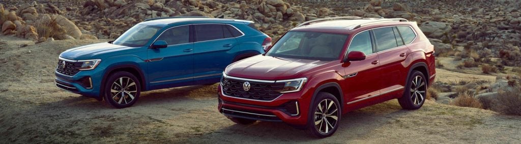 two cars, one blue and one red, are parked next to each other on a cliff overlooking rocks 