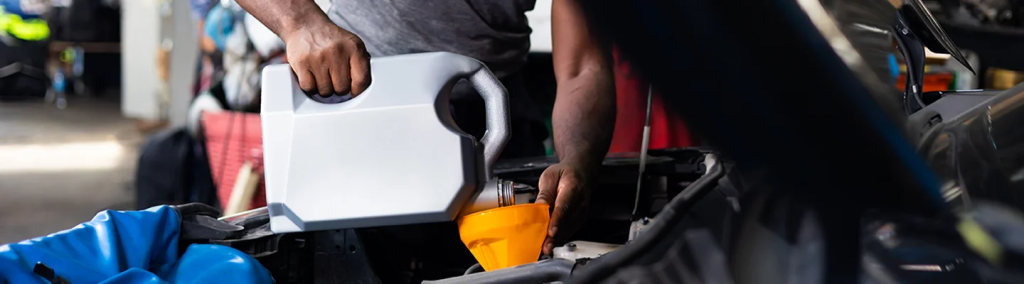 Man pours oil through a funnel in an open car hood 