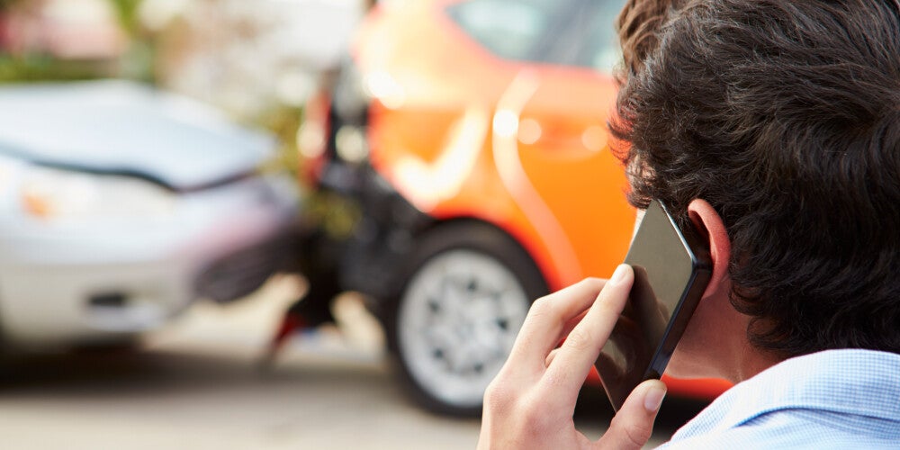 a man is talking on the phone while looking on at a fender bender 