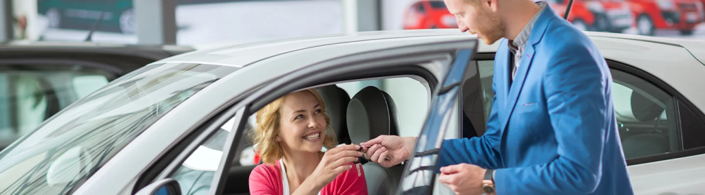 Woman in a car happily accepts keys from car salesman 
