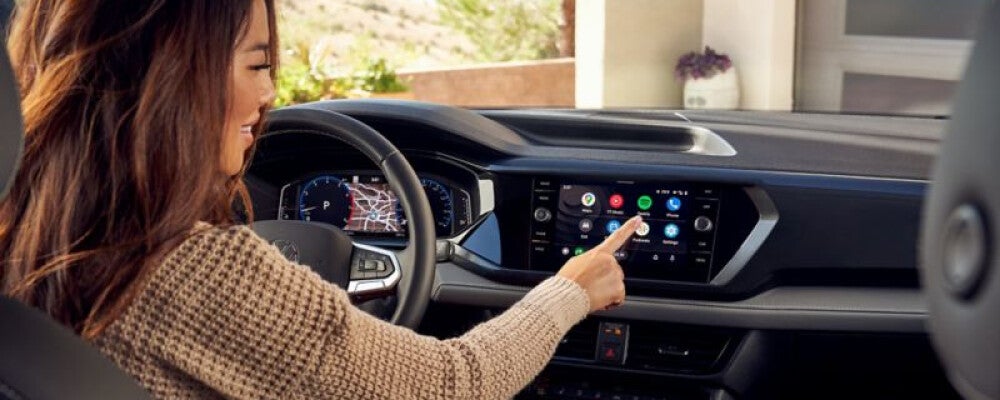 A woman sitting inside of a car presses a button on the touchscreen 
