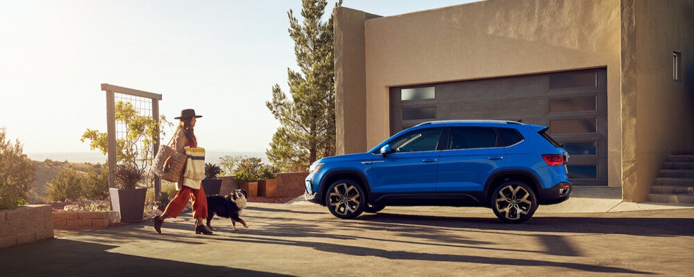 a woman walks with a dog at sunset towards a blue volkswagen 