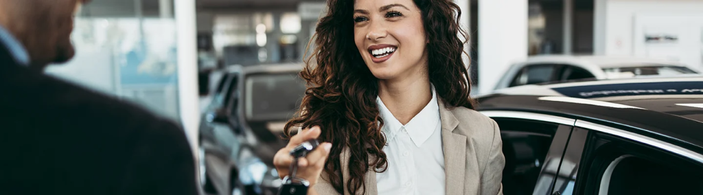 Woman with long dark hair holds out car keys while smiling at a male figure 