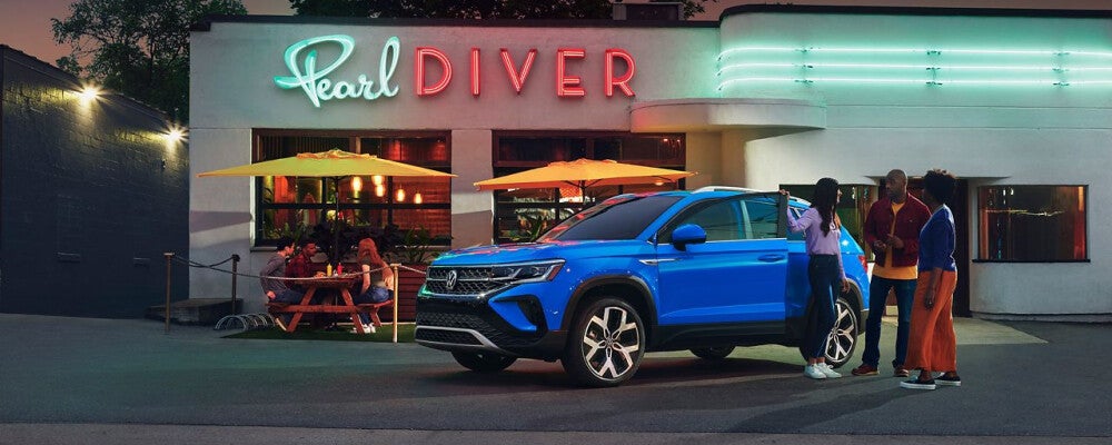 a group of people hanging out in front of a diner that a blue volkswagen is parked in front of 