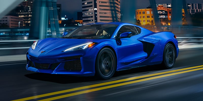 A blue 2026 Chevrolet Corvette sports car driving on a bridge at night.