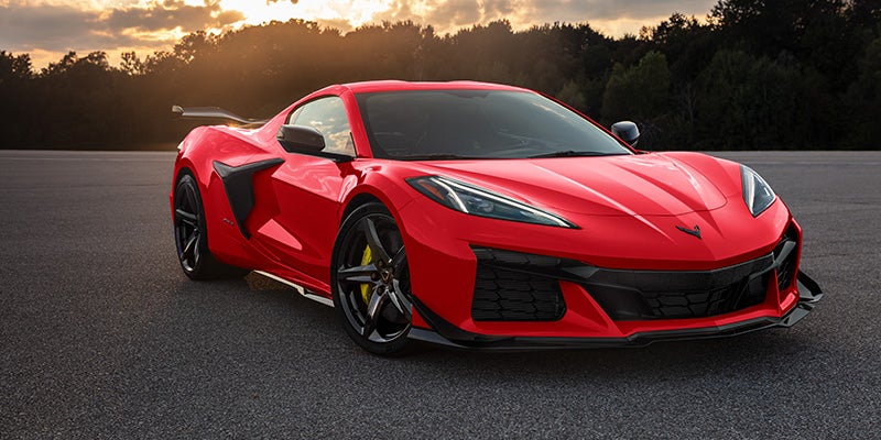 Bright red Chevrolet Corvette Z06 parked on an open road at sunset, showcasing a low aerodynamic design, sharp front styling, and performance wheels.
