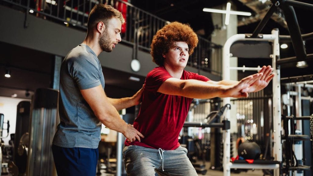 a personal trainer corrects the squatting posture of a young man 