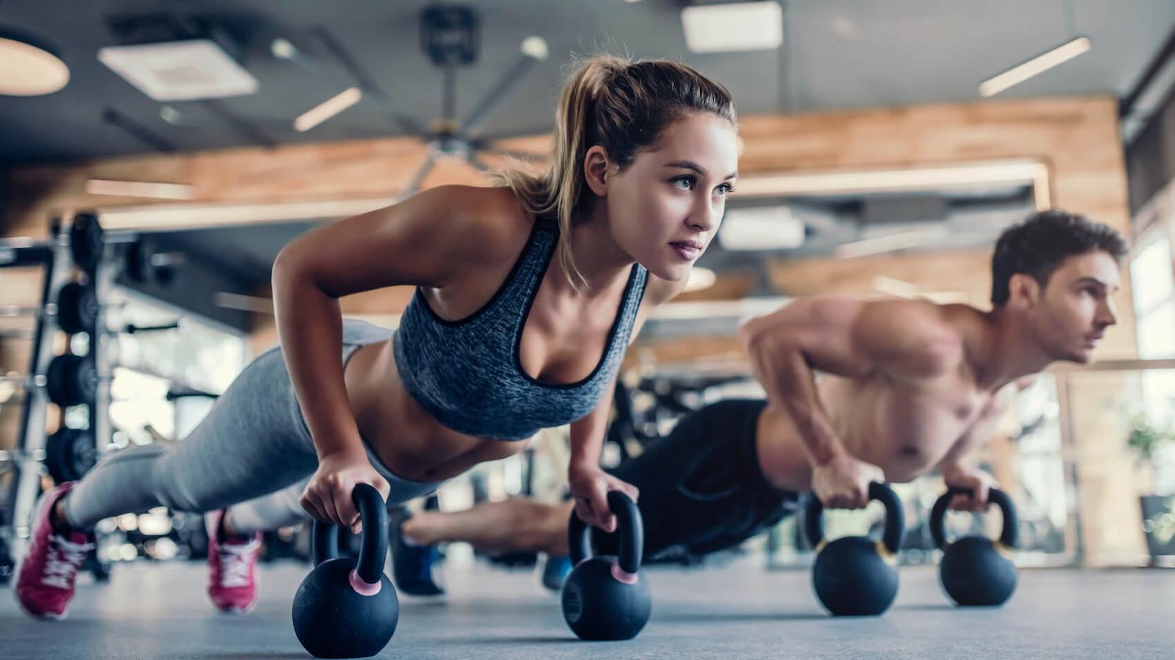 a blonde woman working out doing kettlebell pushups next to a man doing the same exercise 