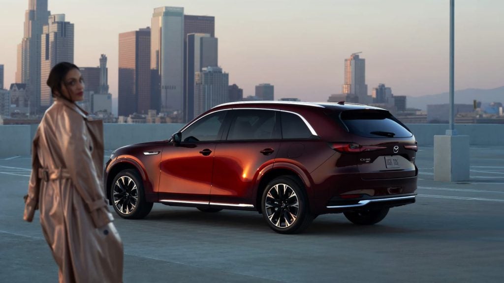 Red Mazda CX-90 parked on a rooftop with a city skyline.
