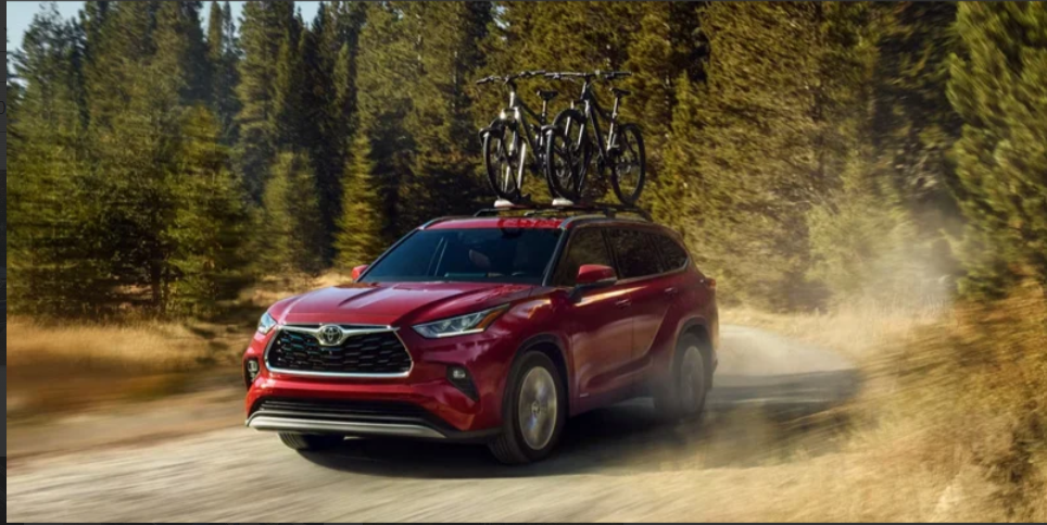 Red Toyota Highlander SUV driving on a forest trail with bicycles mounted on the roof.