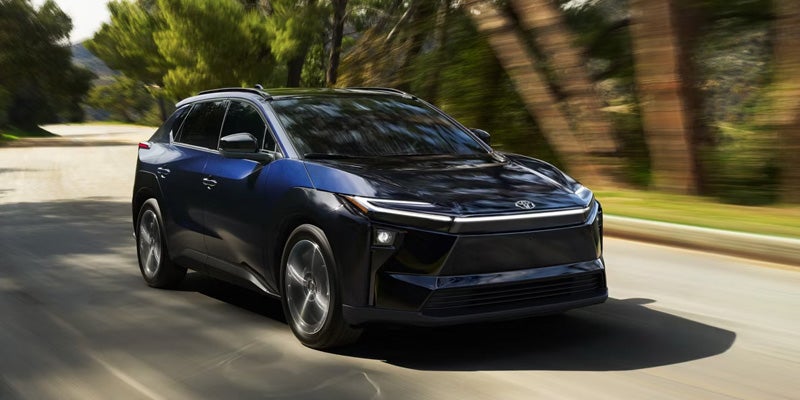 2026 Toyota bZ electric SUV driving on a tree-lined road, showcasing its futuristic design and all-electric performance.