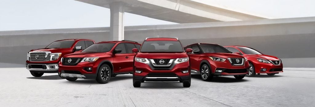 Front view of a lineup of red Nissan vehicles displayed together in a modern outdoor setting, showcasing multiple SUV and sedan models in a coordinated promotional arrangement.