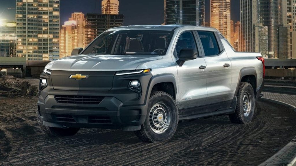 a large silverado EV parked in a dirt area in front of a brightly lit city at night 