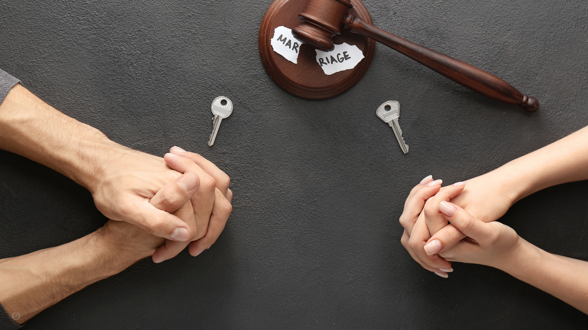 an overhead shot of two pairs of hands clasped toggether on a table with a key in front of both hands