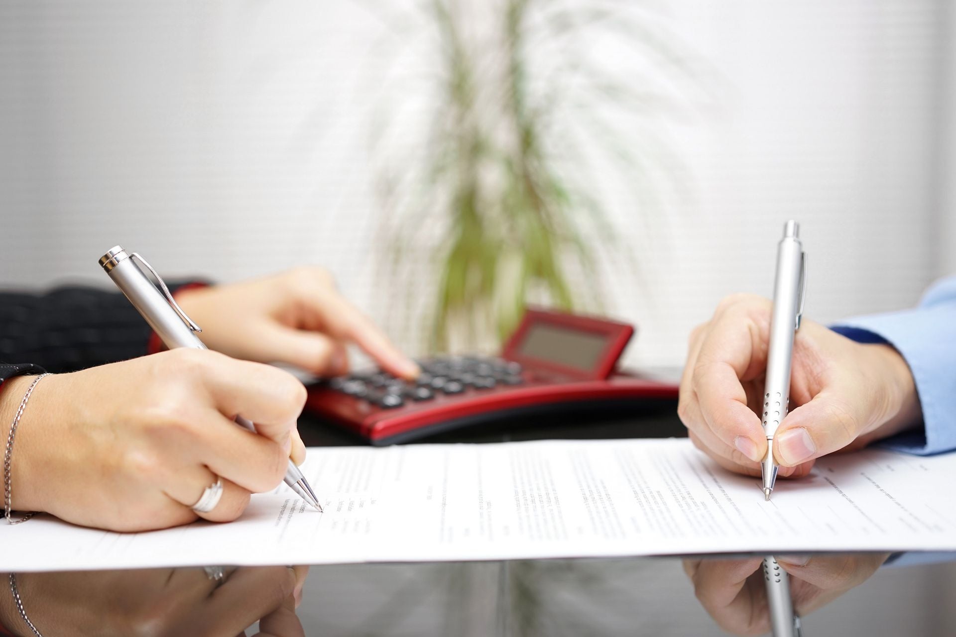 a close up shot of two peoples hands as they fill out paperwork together