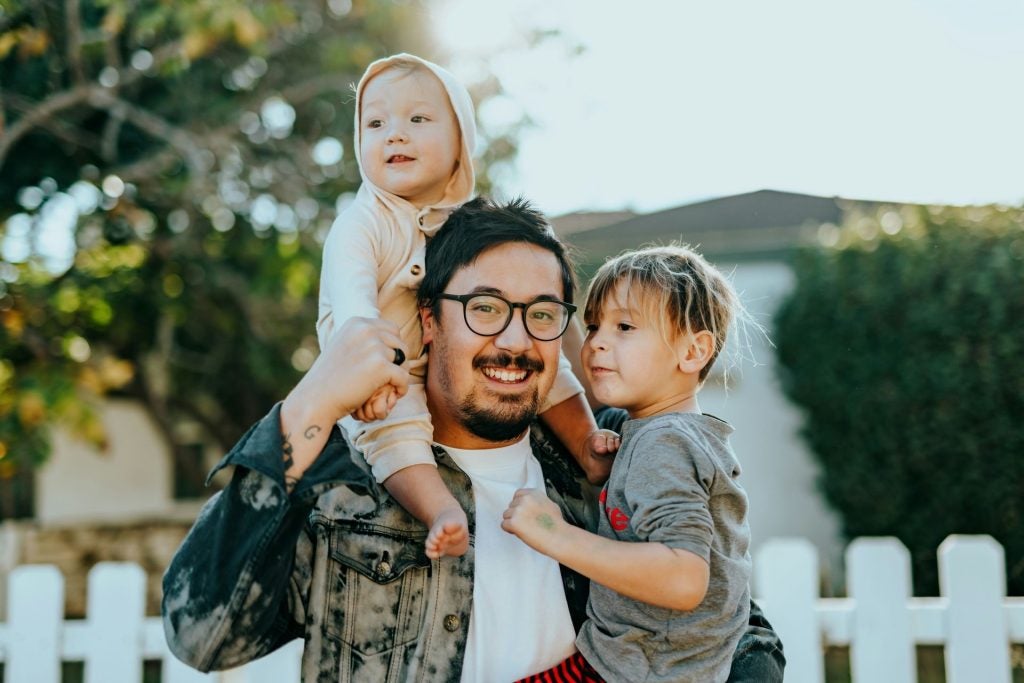 a man holds a child in his arms and another on one shoulder 