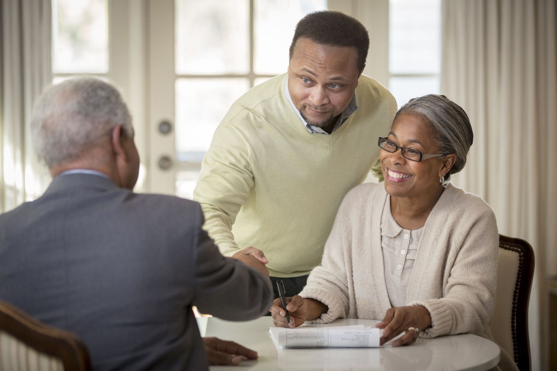 an African American couple sign papers and smile at a lawyer sitting across from them