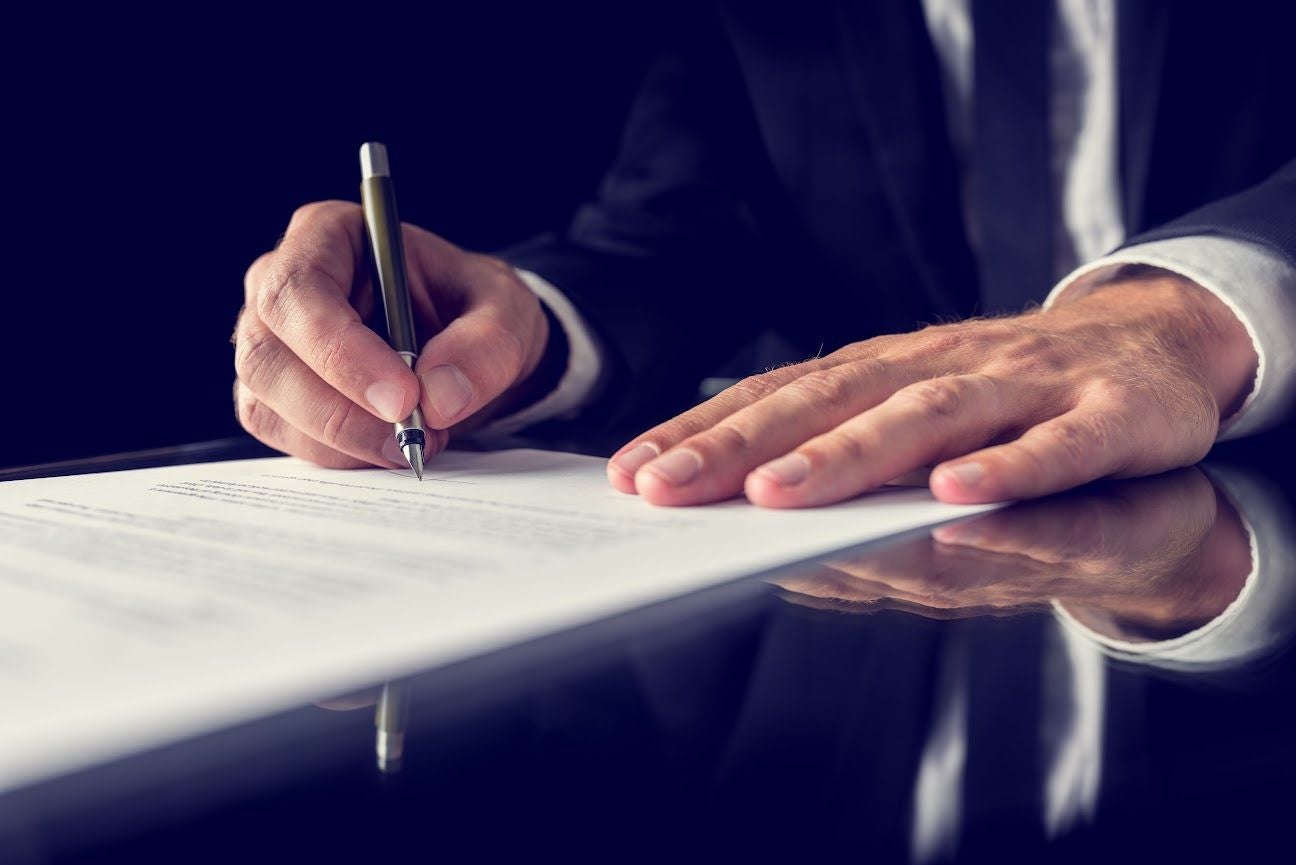 a close up of a mans hands as he signs paperwork