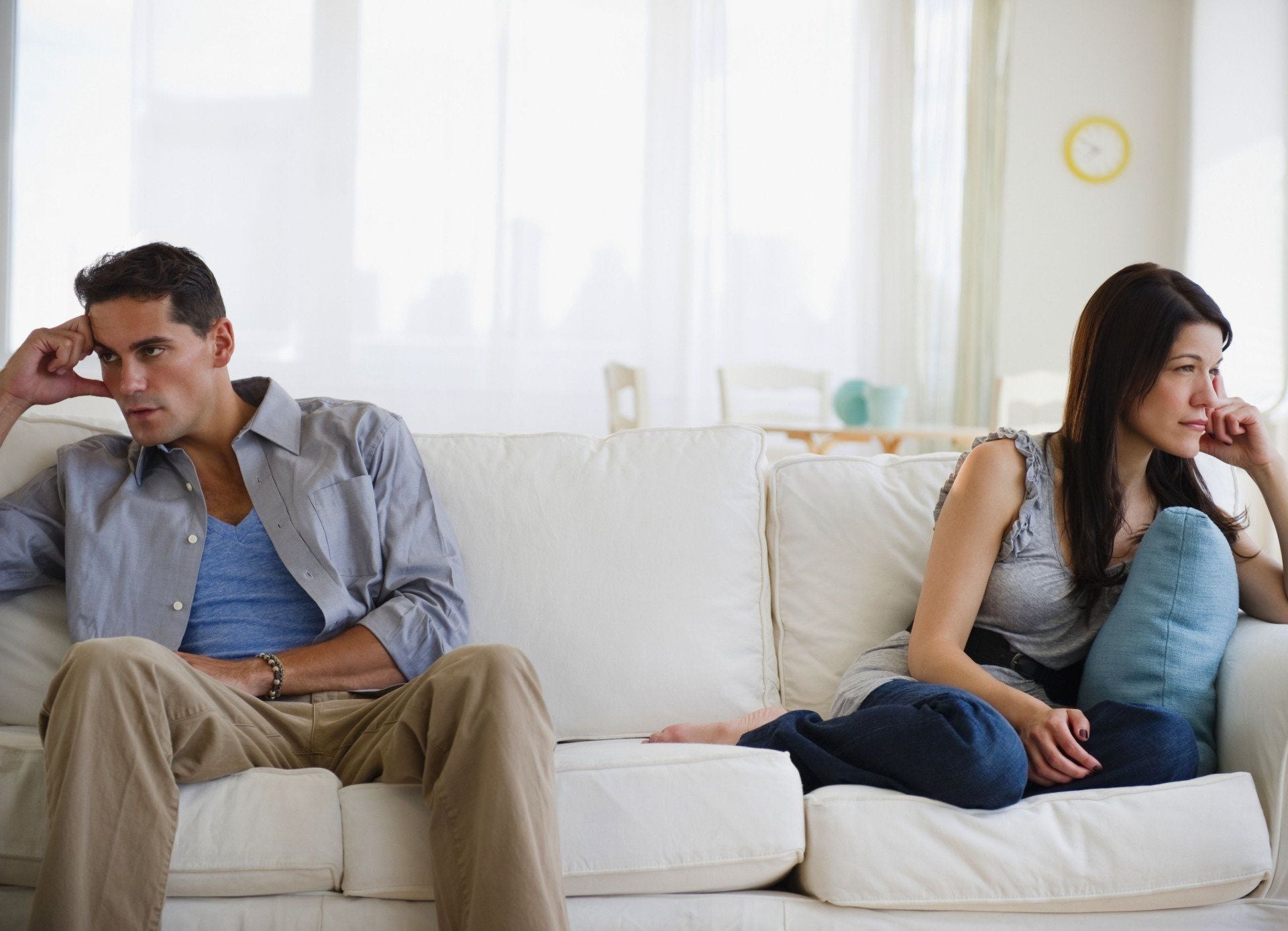a man and a woman sit on the same couch but face away from each other both looking frustrated