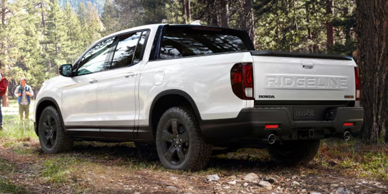 2026 White Honda Ridgeline parked in between forest in its side back profile