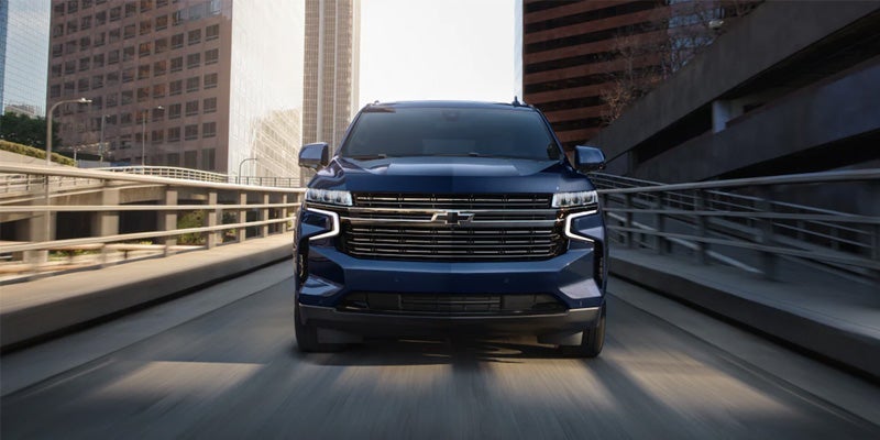 Front grill view of a blue 2024 Chevrolet Tahoe driving through a city