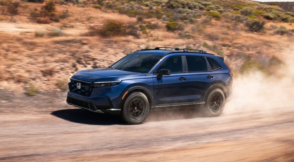 Blue 2026 Honda CR-V driving off-road on a dirt trail.