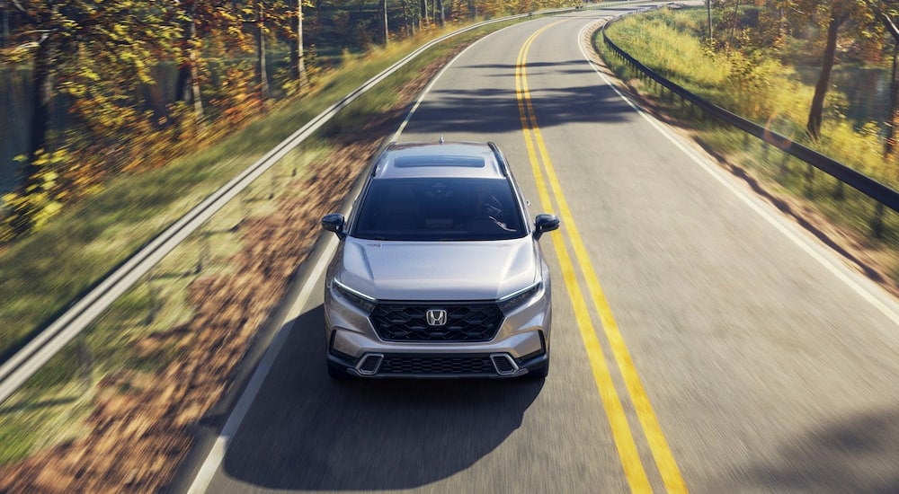 White 2026 Honda CR-V Sport Touring Hybrid driving down an open road.