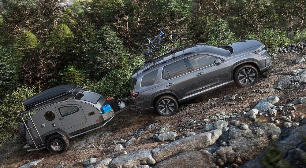 Grey 2025 Honda Pilot Sport towing a camper up a hill.