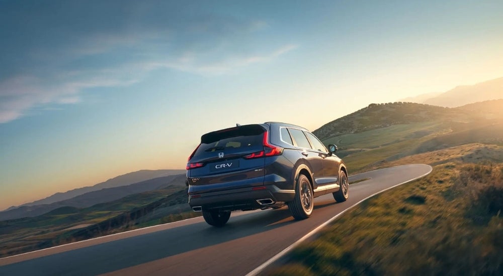 Rear view of a blue 2025 Honda CR-V Hybrid driving down a scenic road
