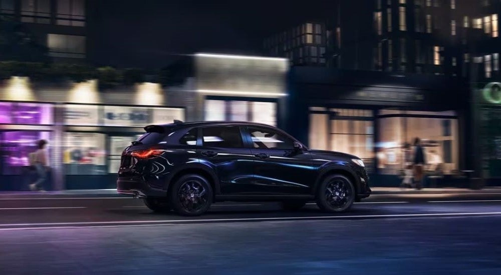 Rear view of a black 2025 Honda HR-V Sport driving through a city at night.