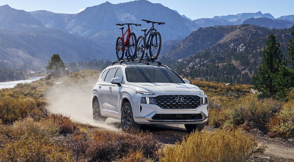 A white 2022 Hyundai Santa Fe driving down a dirt road from a dealer with used cars for sale.