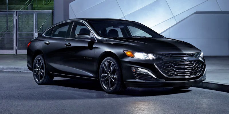 Front three-quarter view of a 2022 black sedan parked on a city street at night, featuring modern styling, illuminated headlights, and a sleek chrome-accented grille.