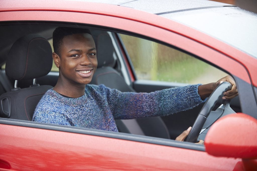Young driver sitting inside a red car with hands on the steering wheel