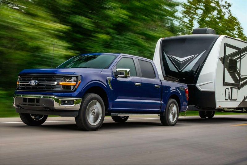 Blue Ford F-150 pickup truck towing a travel trailer on the road