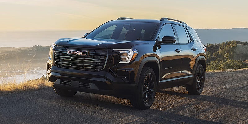 Black GMC Terrain SUV parked on a coastal hillside road at sunset.